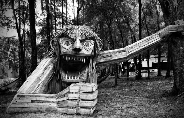 A black and white image of a big wooden troll found in the forest. The troll's mouth filled with jagged teeth is open in a silent scream.
